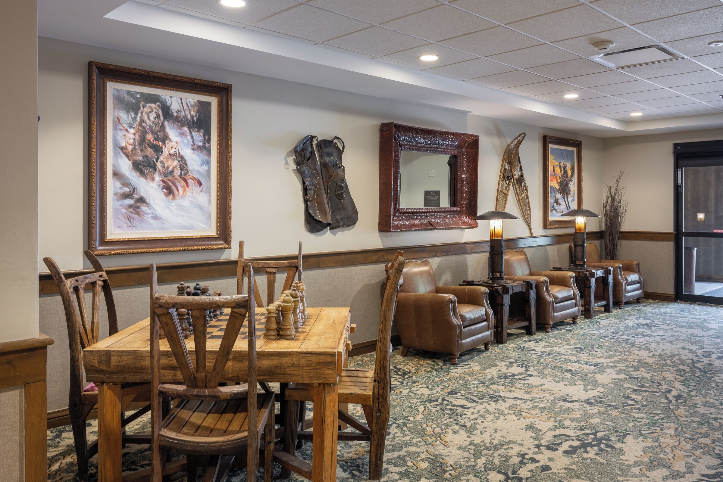 A room with a wooden table and chairs, a brown leather sofa, and framed artwork on the walls.
