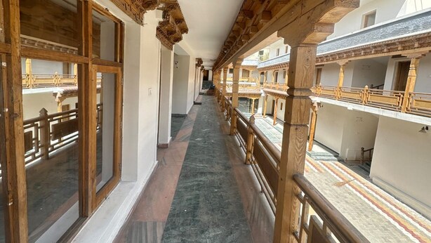 A corridor with wooden railings, large windows, and a view of the courtyard below. - Hotel Dimbir Regency (Leh)