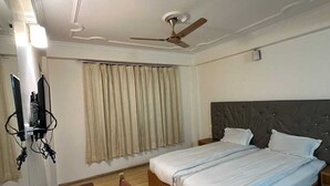 A hotel room with a bed, a ceiling fan, a desk with a chair, and a television. - Hotel Dimbir Regency (Leh)