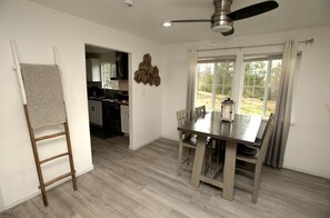 Ein Essbereich mit Tisch und Stühlen, einem Deckenventilator und Blick ins Freie durch große Fenster.
