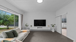 A modern living room with a large flat-screen TV, a grey carpet, and a white sofa with cushions.