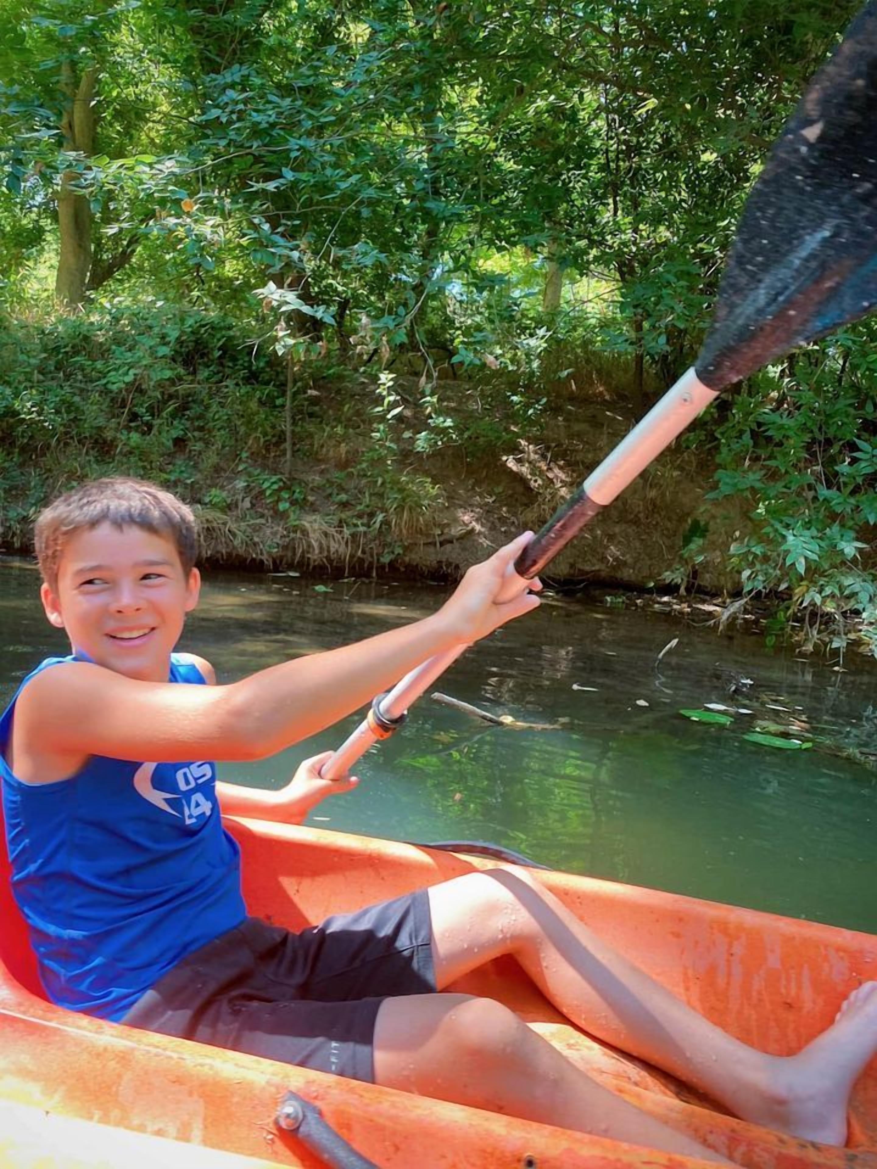 A person in a canoe on a river surrounded by greenery.