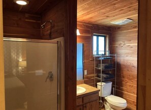 Ein Badezimmer in einer Holzhütte mit Duschabtrennung aus Glas, Toilette, Waschbecken und Ablagefläche mit gefalteten Handtüchern.