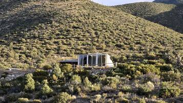 A modern building with large windows, situated on a hillside with sparse vegetation.