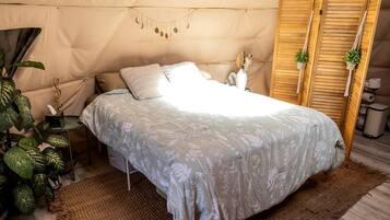A tented room with a bed, a small table with a plant, and a wooden wardrobe.