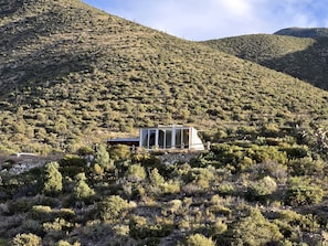 Un edificio moderno con grandes ventanales, ubicado en una ladera con vegetación escasa.