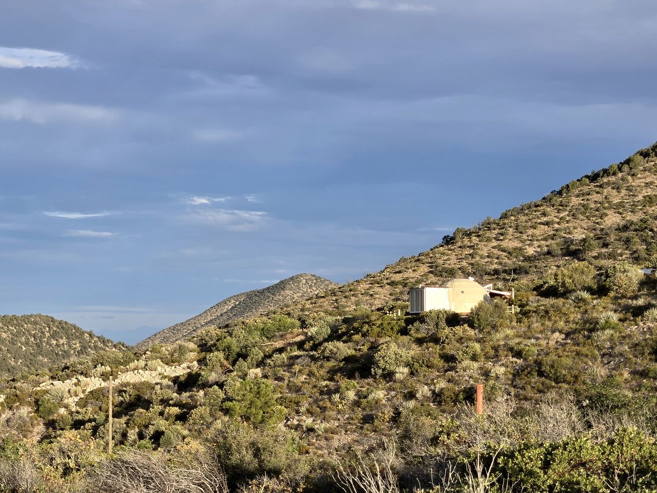 A mountainous landscape with sparse vegetation and a small building on a hill.
