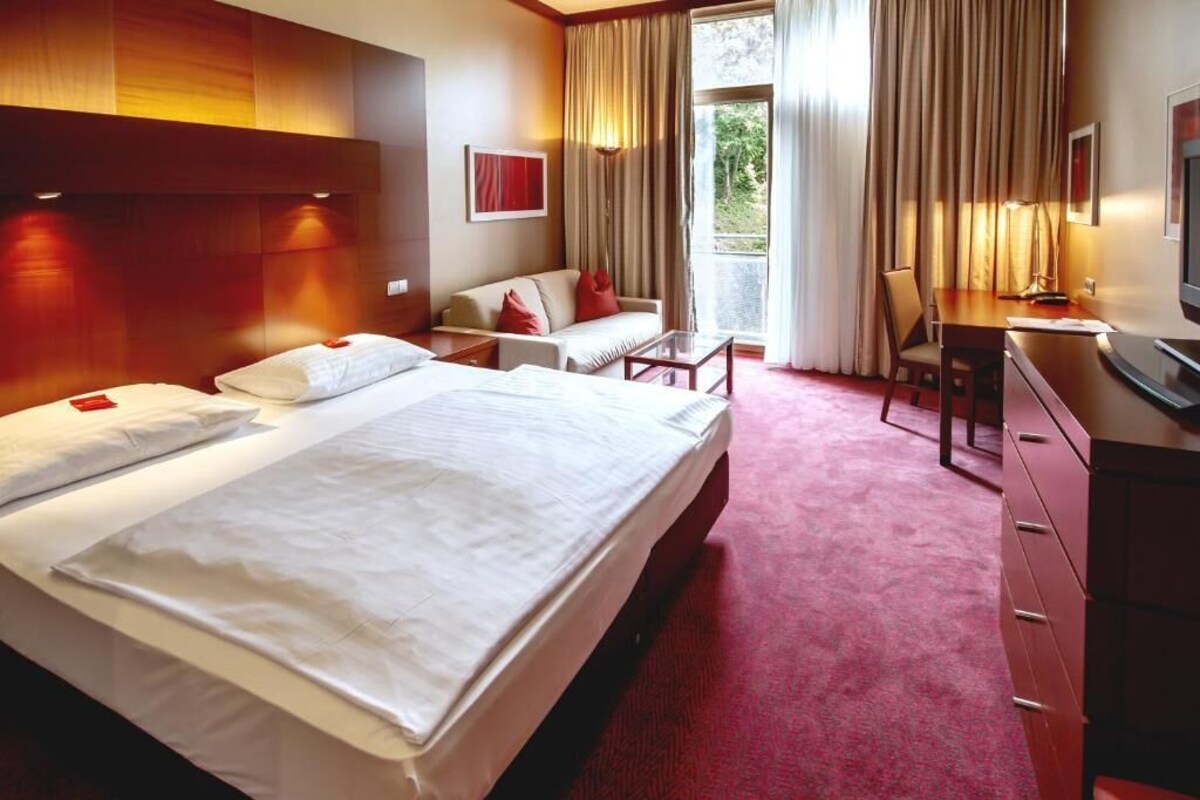 A hotel room with a large bed, a desk, a chair, and a TV.