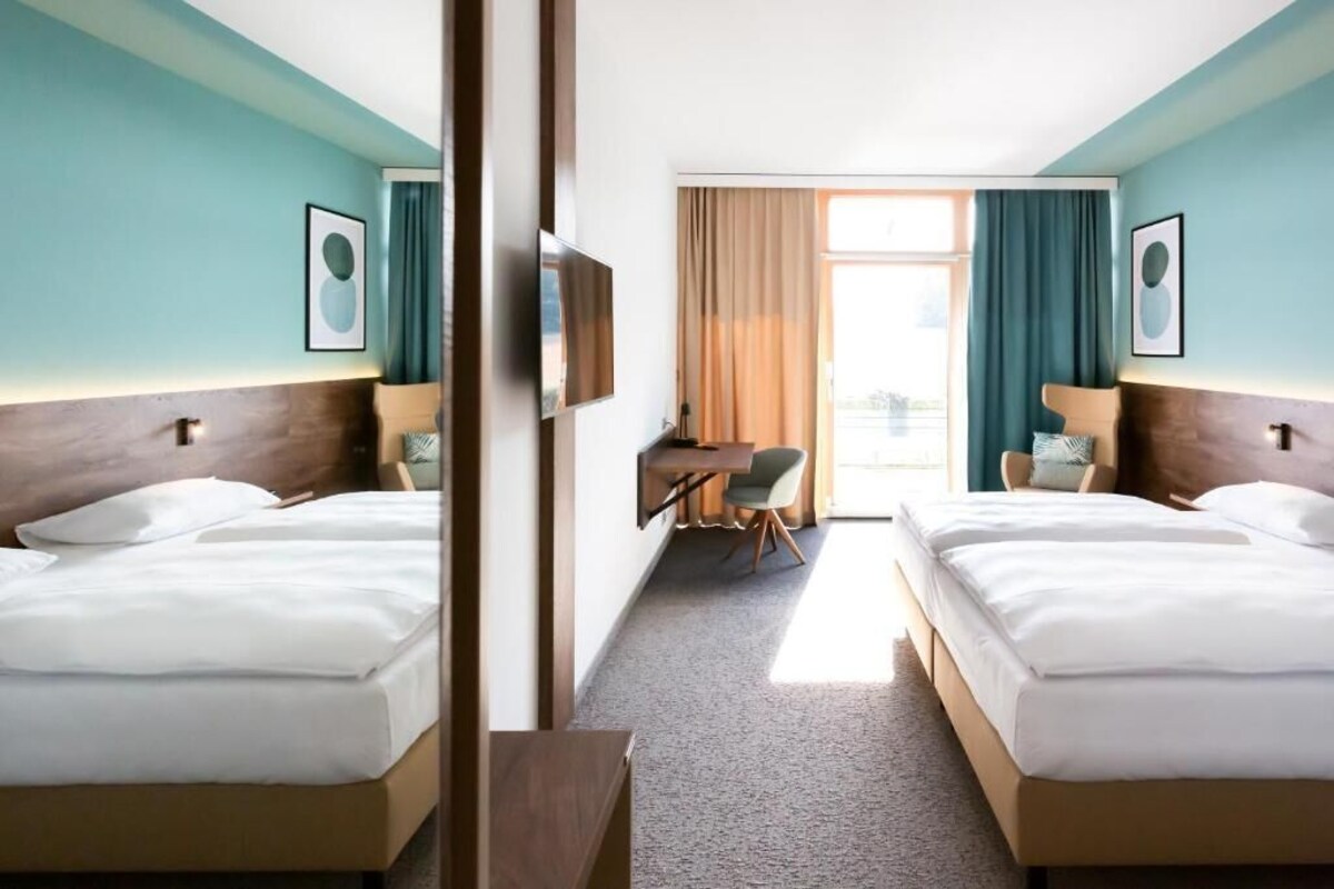 A hotel room with two beds, a desk, a chair, and a TV.