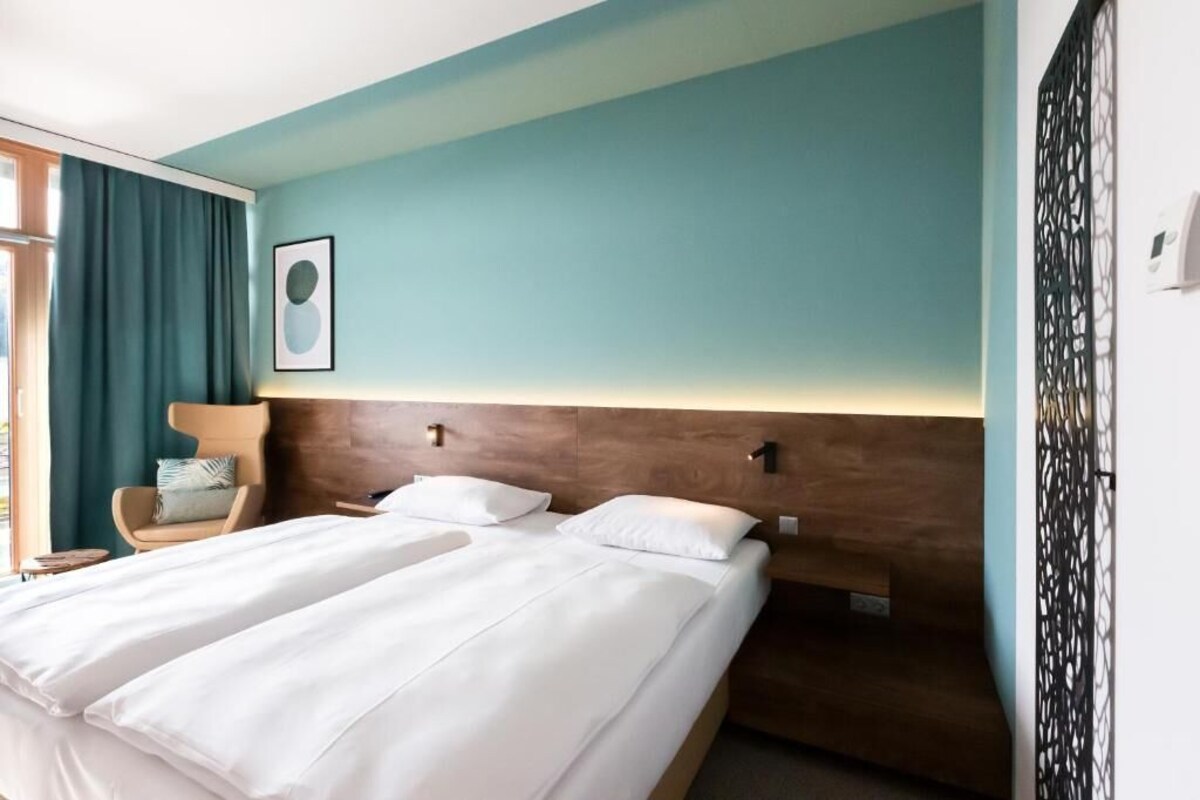 A hotel room with a bed, a chair, and a window with curtains.