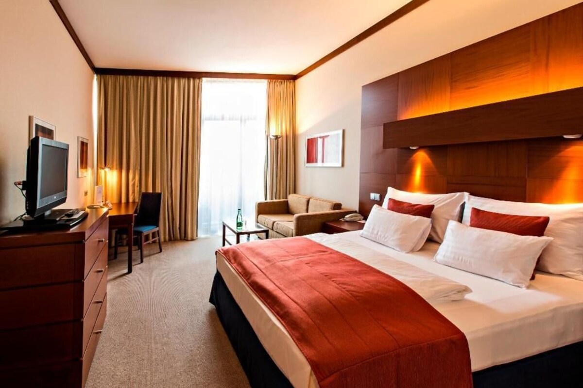 A hotel room with a bed, a desk, a chair, a television, and a window with curtains.