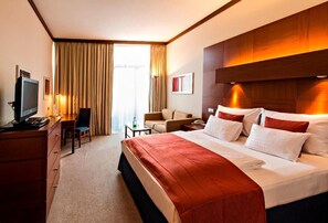 A hotel room with a bed, a desk, a chair, a television, and a window with curtains. - Hotel Das Sonnreich (Bad Loipersdorf)