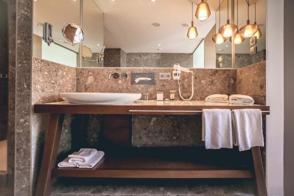 A modern bathroom with a marble vanity, a large mirror, a sink, a handheld showerhead, and a towel rack.
