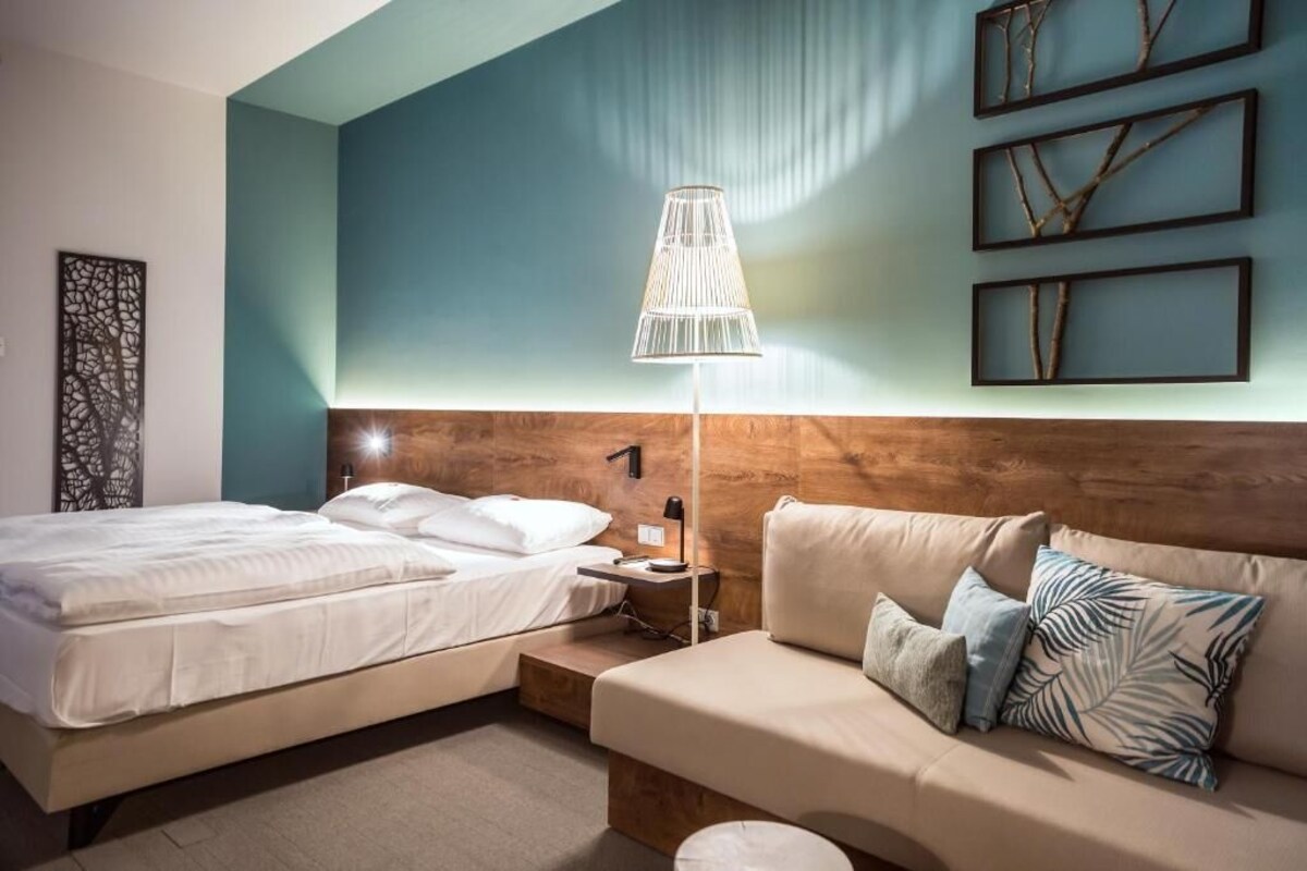 A hotel room with a bed, a sofa, a lamp, and wall art.