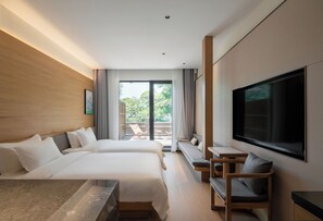 Habitación de hotel con dos camas, televisor, zona de estar y balcón con mobiliario exterior.