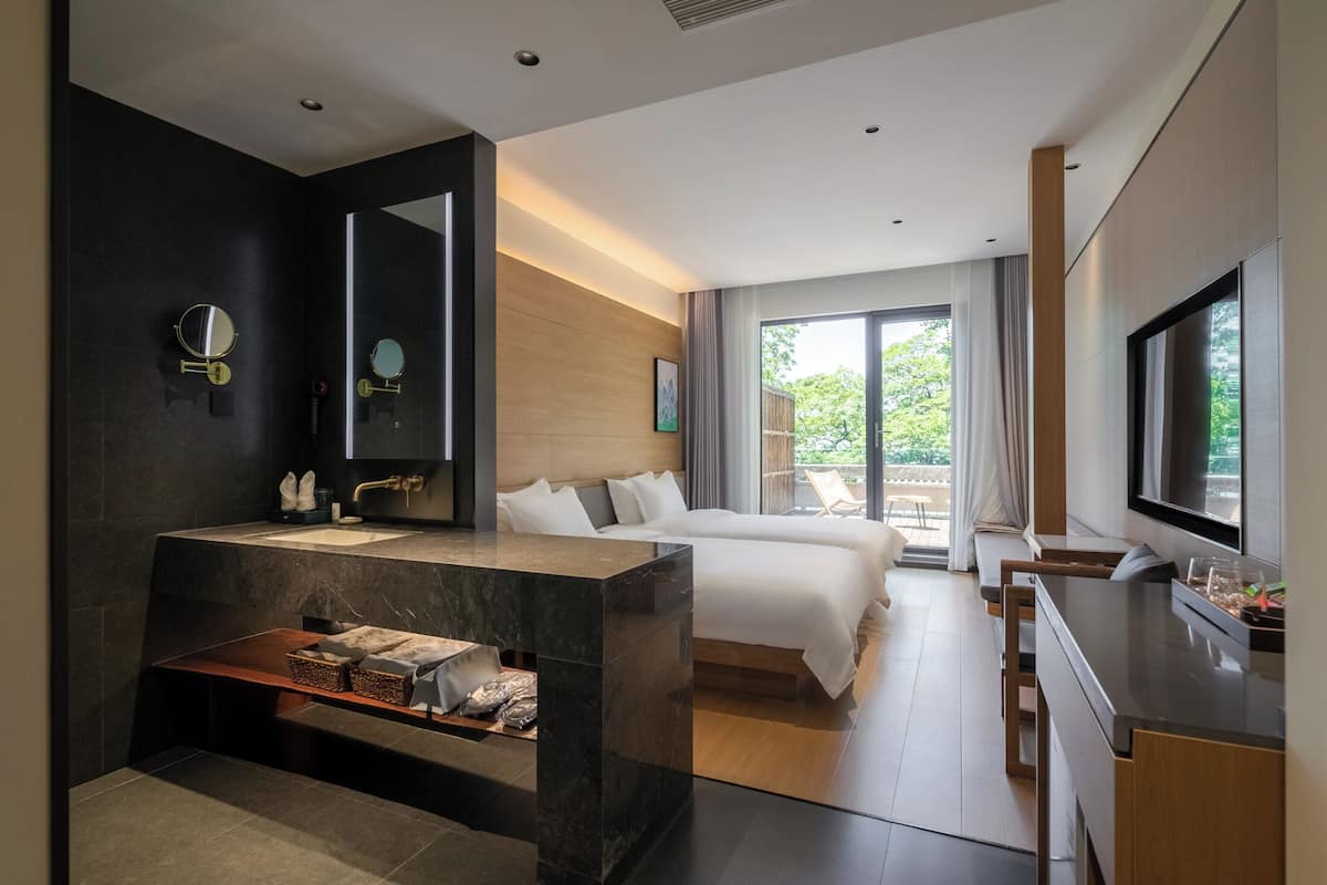 Une chambre d’hôtel moderne dotée d’un grand lit, d’une salle de bain avec un meuble-lavabo, d’une télévision et d’un balcon offrant une vue agréable.