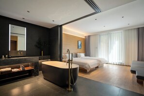 Una habitación de hotel moderna con una bañera grande, una cama, un sofá y un ventanal con cortinas.