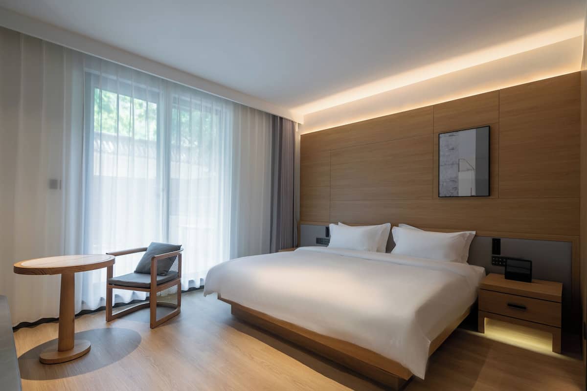 Une chambre d’hôtel moderne avec un grand lit, des tables de chevet, une petite table ronde et une chaise.