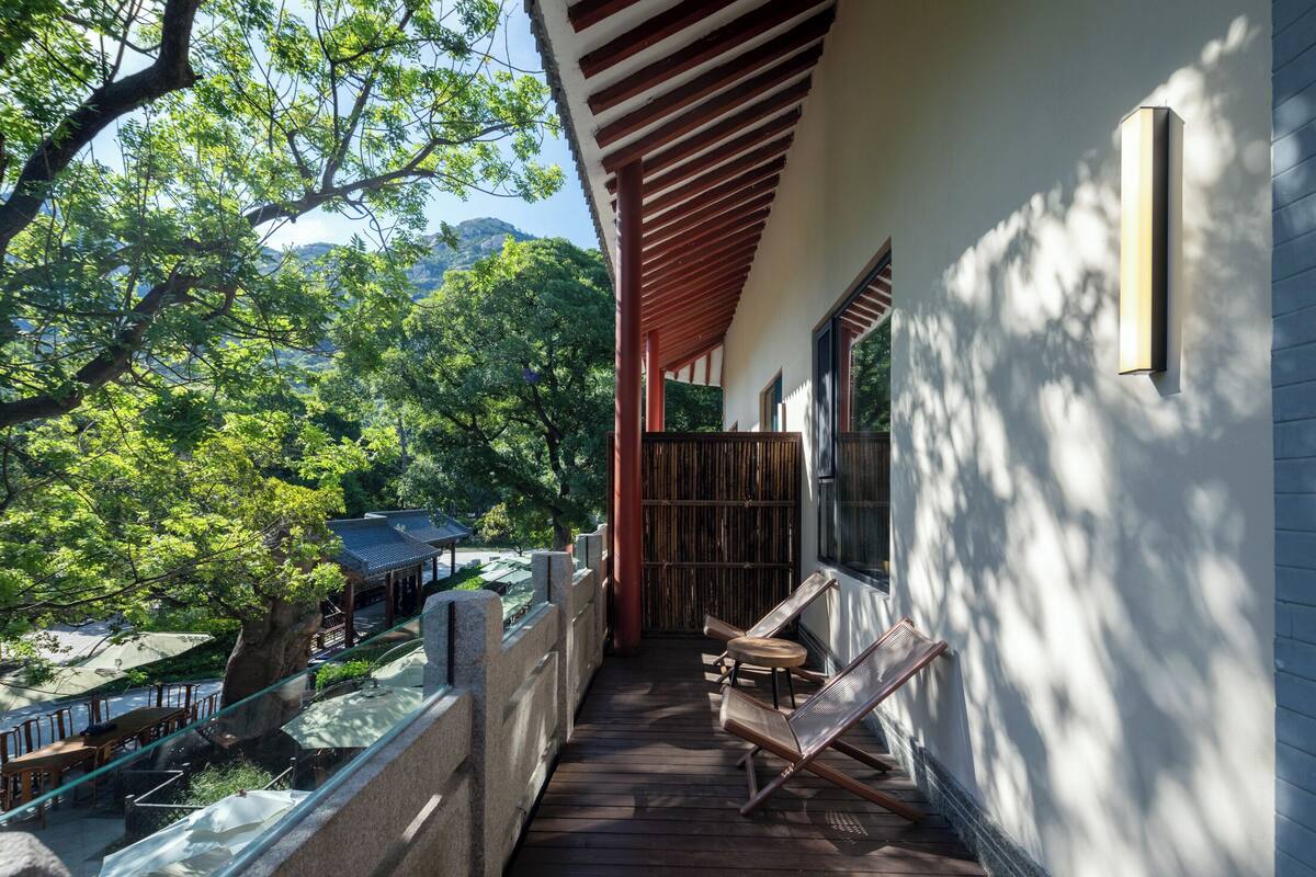Une terrasse en bois offrant une vue sur une montagne et des arbres, un espace salon couvert et un bâtiment à l’extérieur blanc.