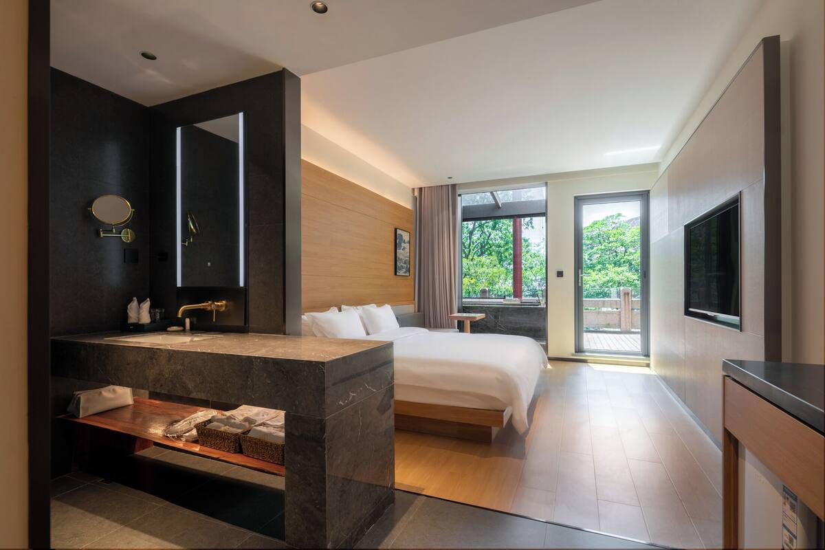 Une chambre d’hôtel moderne dotée d’un grand lit, d’une salle de bain avec un miroir et un lavabo, et d’un téléviseur fixé au mur.