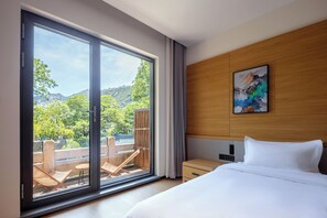 A hotel room with a large sliding glass door leading to an outdoor balcony, a bed with white linens, a wooden headboard, and a painting on the wall. - A Thought Laoshan Cultural Experience (Qingdao)