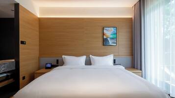 A modern hotel room with a large bed, wooden panel walls, a painting, a bedside table with a phone, and a TV.