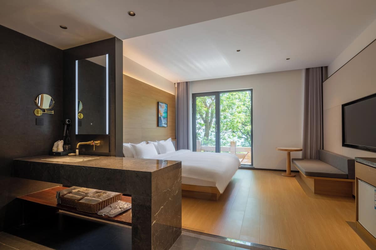 Une chambre d’hôtel moderne dotée d’un grand lit, d’un coin salon, d’une télévision et d’une salle de bain avec un meuble-lavabo en marbre.