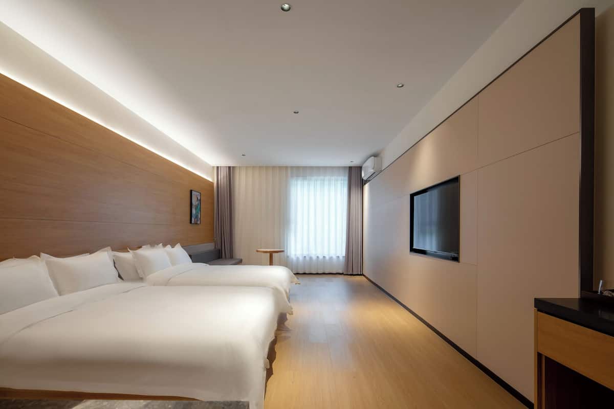 Une chambre d’hôtel avec deux lits, un téléviseur à écran plat, une petite table et une fenêtre avec des rideaux.