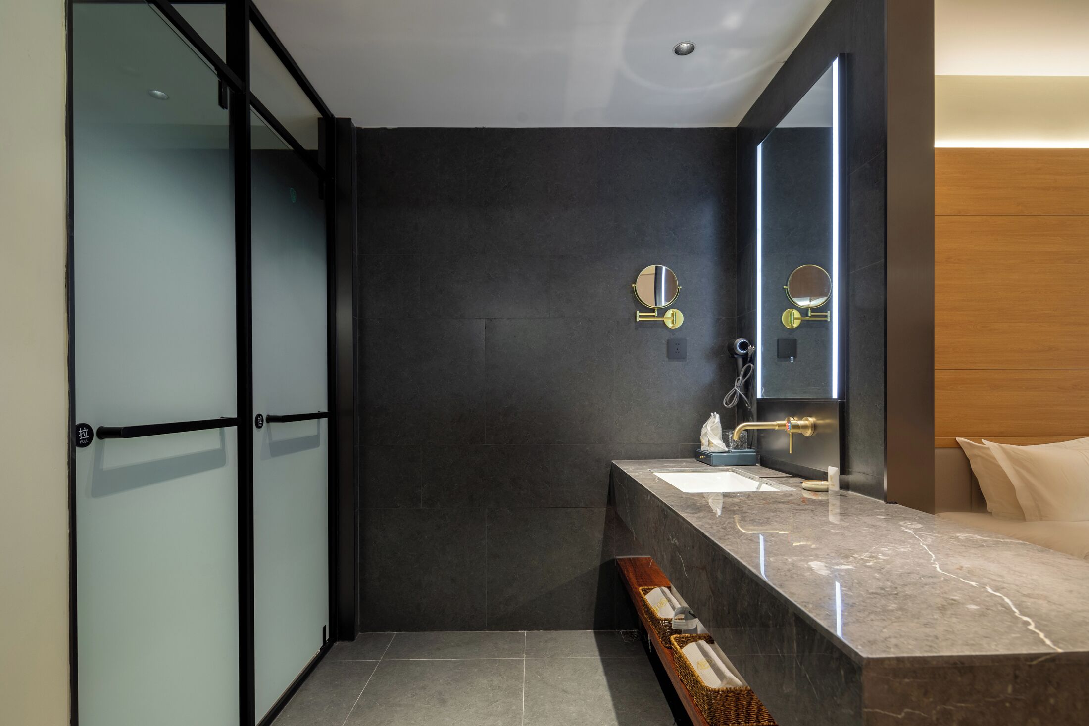A modern bathroom with a dark tiled wall, a marble sink, and a large mirror.