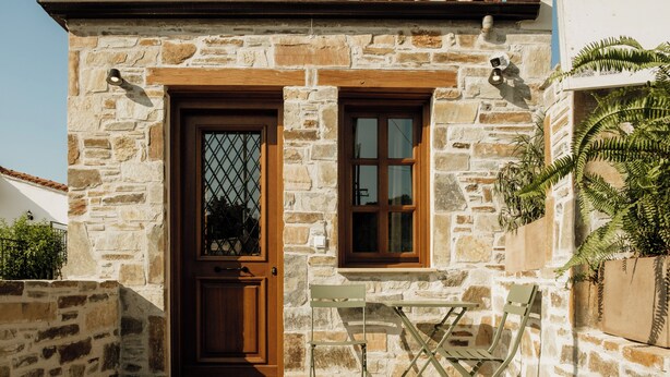 A stone building with a wooden door, a window, and a small table with chairs. - Galetso Stone Studio by Still Collection (Νικήτη)