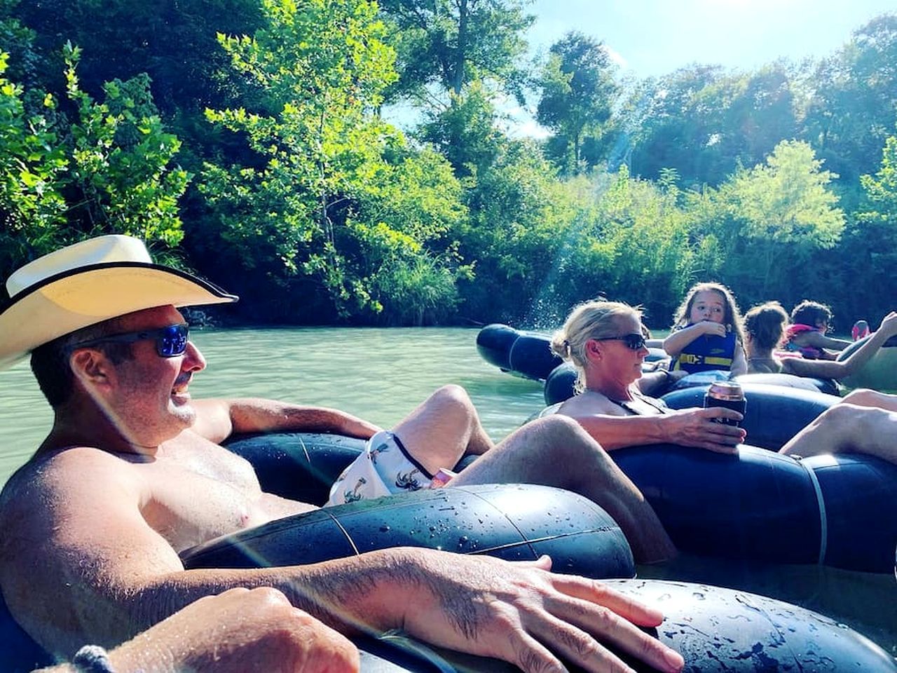 People on inflatable tubes in a body of water surrounded by greenery.