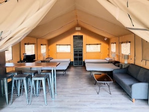 A tented accommodation with a central table, bar stools, a sofa, and a bed. - Texas Safari Tent Adventures Await in this Lovely San Marcos River Rental (Kingsbury)