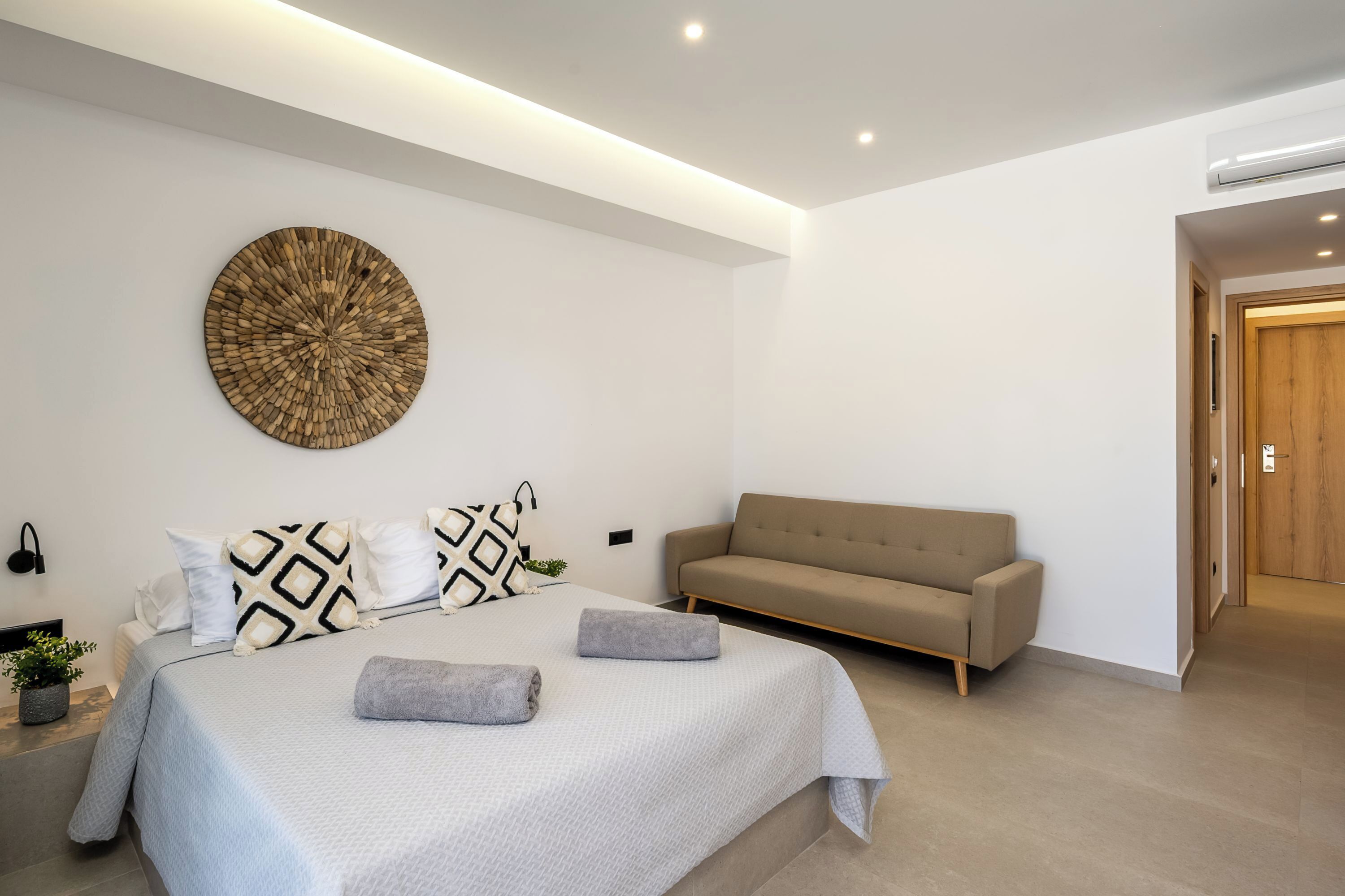 Un dormitorio moderno con una cama, un sofá, una obra de arte en la pared y una puerta.