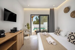 A modern hotel room with a flat-screen TV, a wooden desk with a kettle, a bed with rolled towels, and a view of a pool through a sliding door.