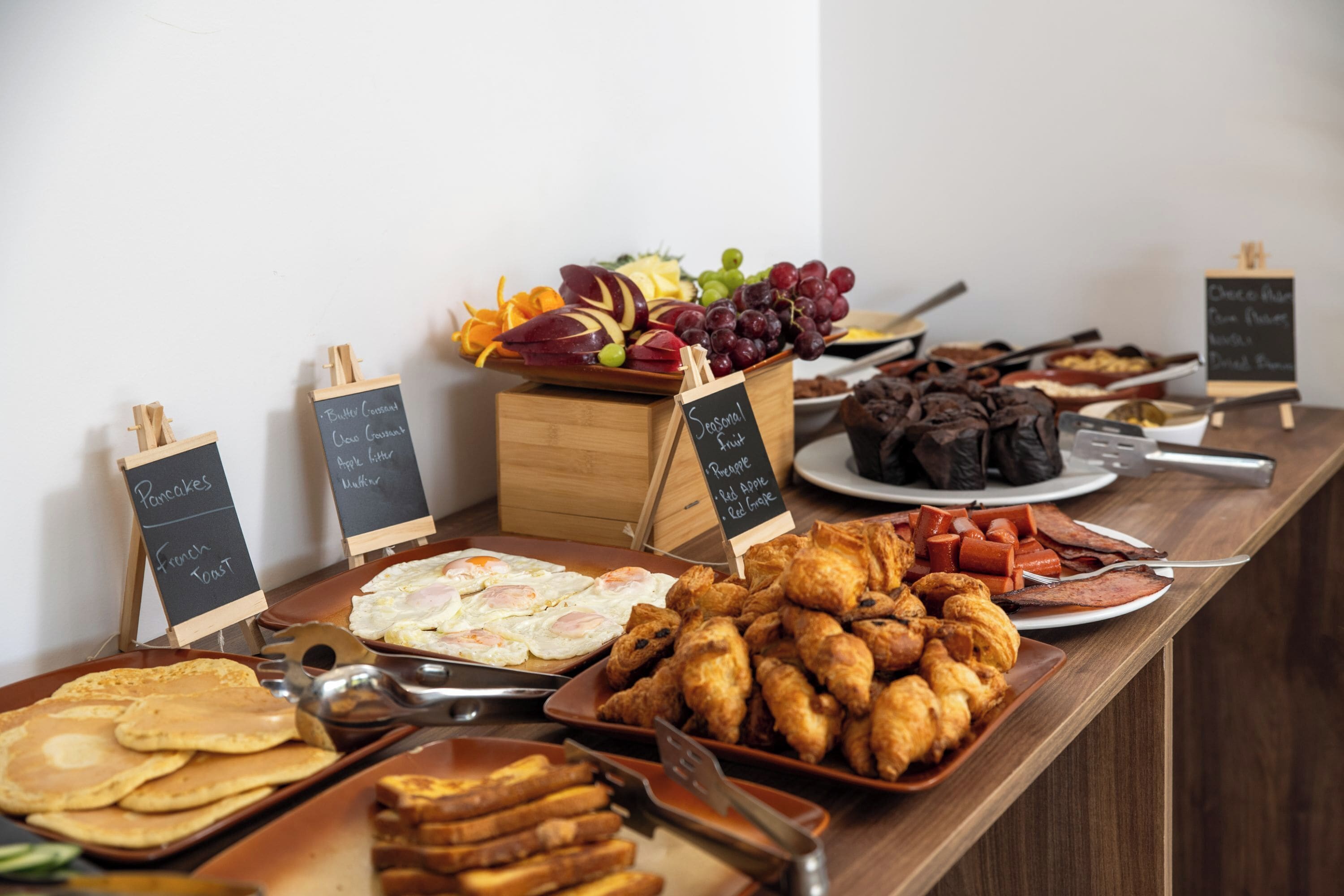 Un buffet proposant une variété de plats, notamment des crêpes, des œufs, des croissants, ainsi qu’un assortiment de fruits et de légumes.