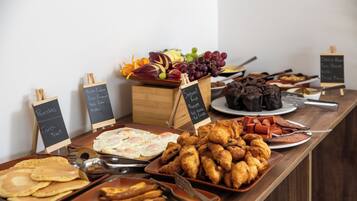 Un buffet proposant une variété de plats, notamment des crêpes, des œufs, des croissants, ainsi qu’un assortiment de fruits et de légumes.