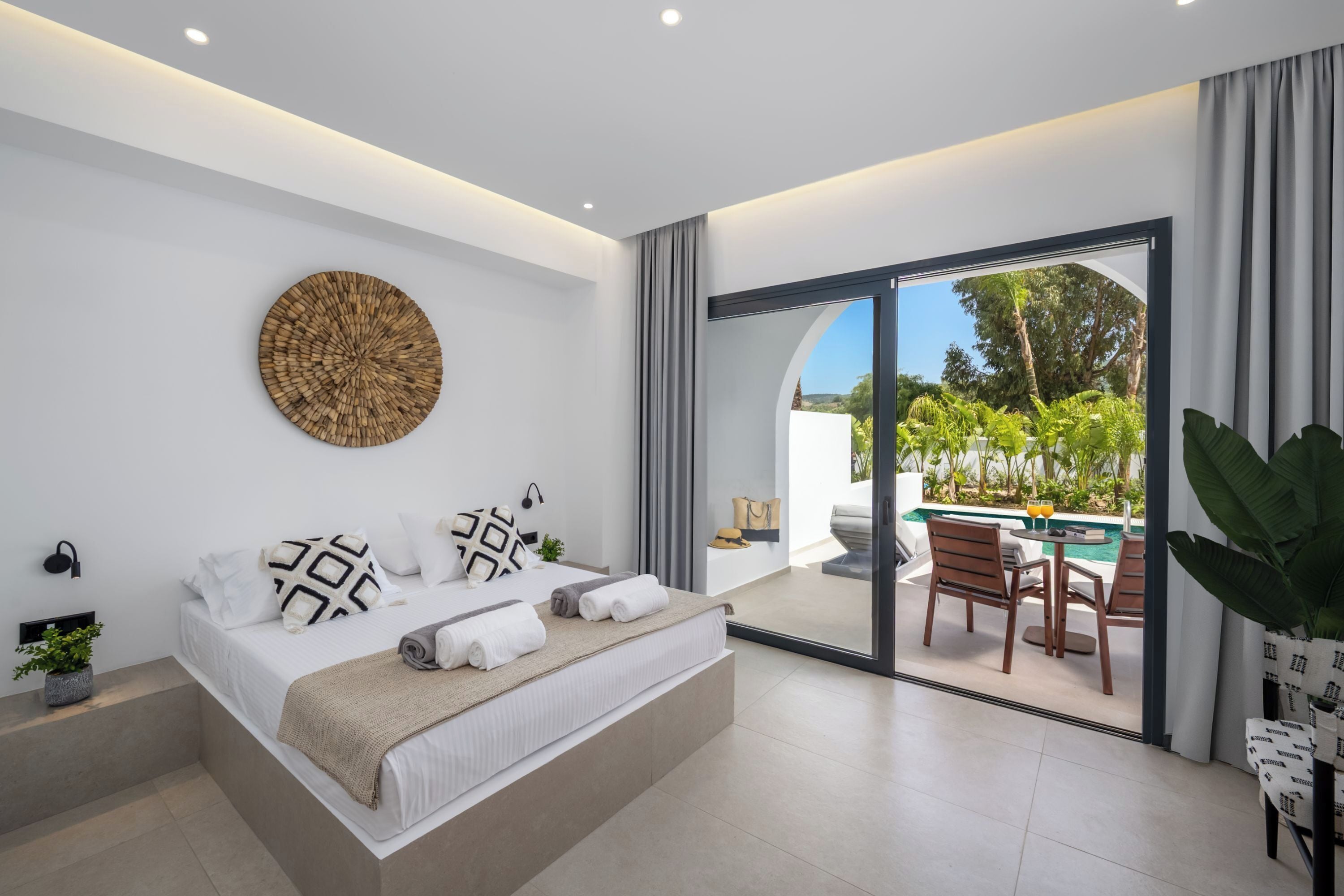 Un dormitorio moderno con una cama grande, una obra de arte circular en la pared y vistas a un patio exterior con piscina y sillas.
