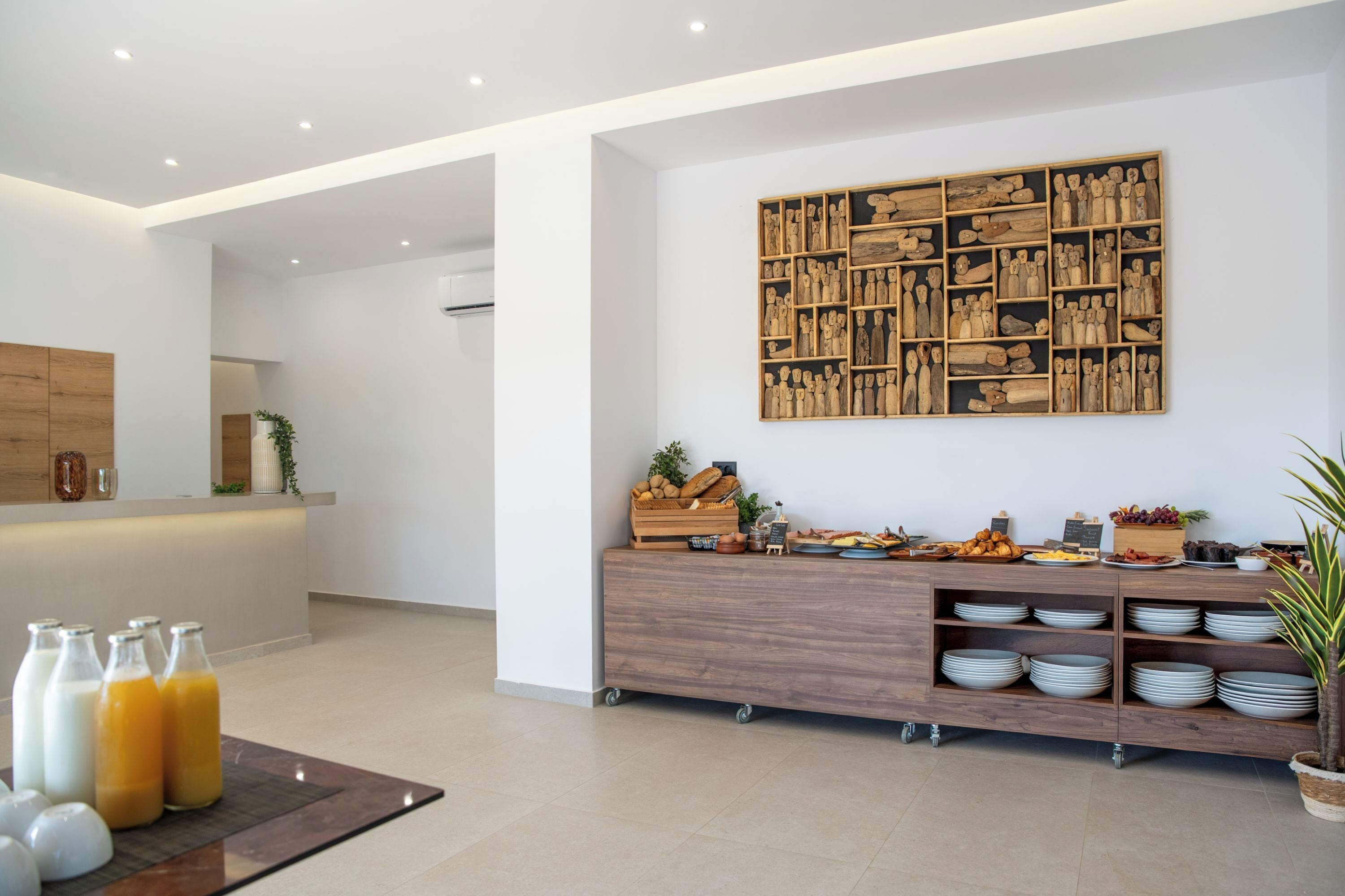 A modern reception area with a wooden reception desk, a wall-mounted sculpture, and a buffet counter with plates and bowls.