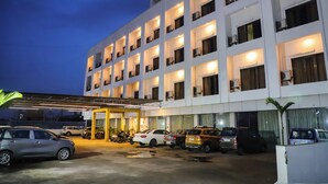 Un hotel de varios pisos con zona de estacionamiento techada y varios autos estacionados en la entrada.
