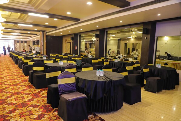 Un salón de banquetes con filas de mesas redondas, cintas amarillas y negras y un piso cubierto de alfombra roja.