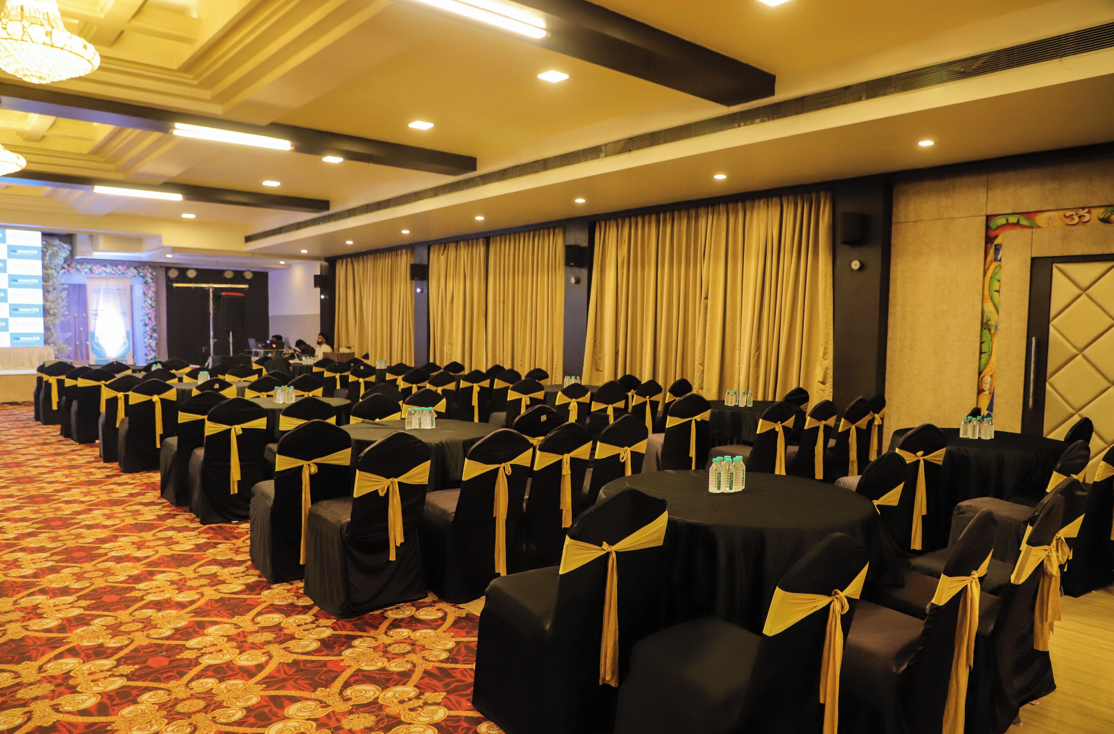 A conference room with rows of tables and chairs, each with black covers and gold sashes.