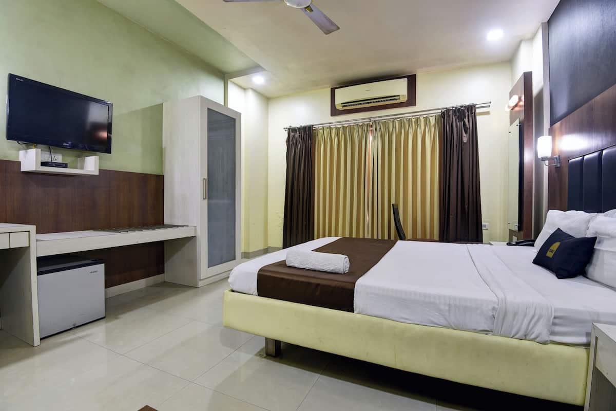 Una habitación de hotel con cama, escritorio con computadora, televisión y aire acondicionado.
