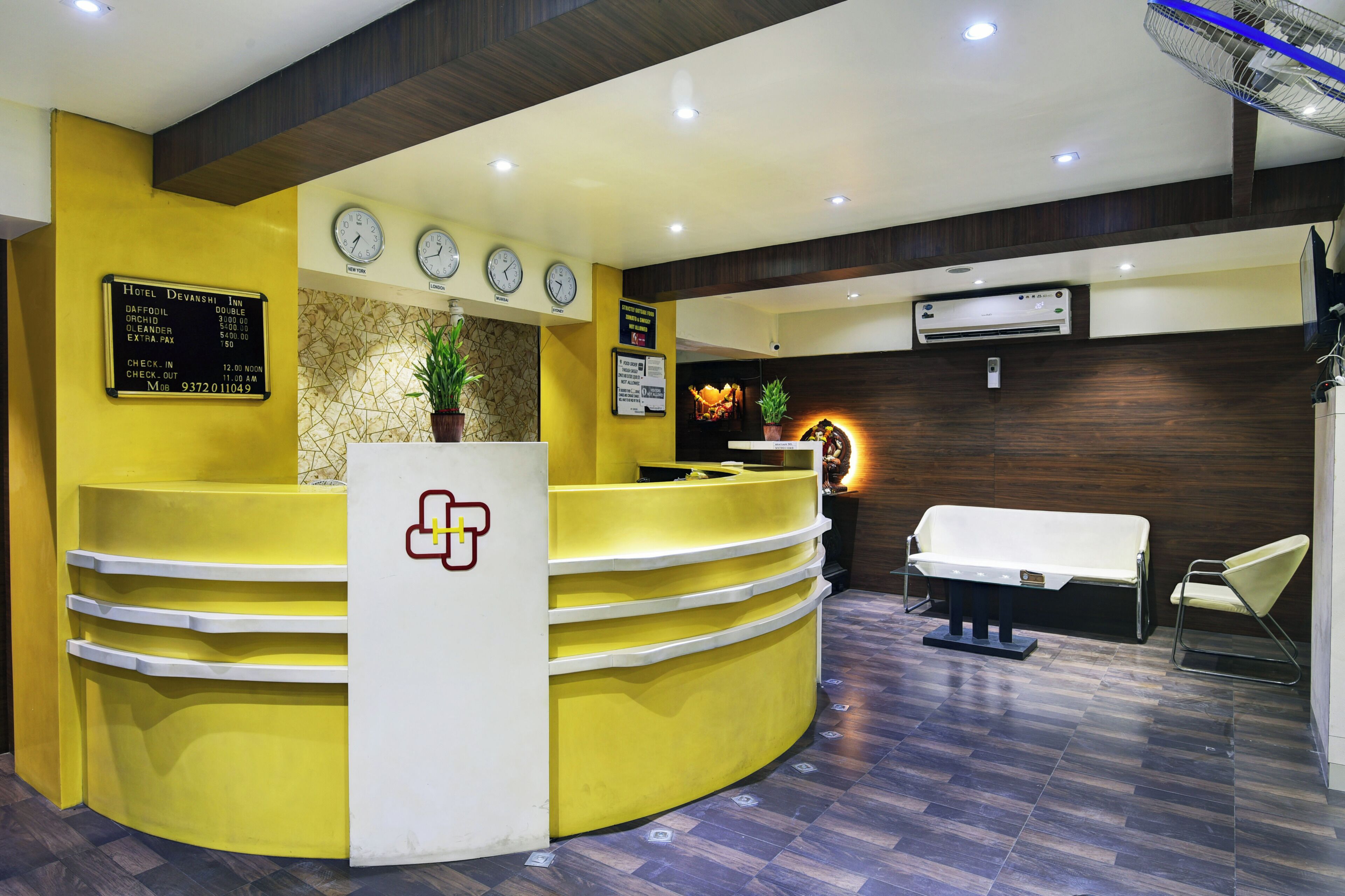 A hotel reception area with a yellow counter, a reception desk, a clock, and a wall-mounted air conditioning unit.