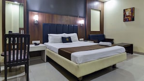 Habitación de hotel con cama, mesitas de noche, una silla, un escritorio y una obra de arte colgada en la pared.