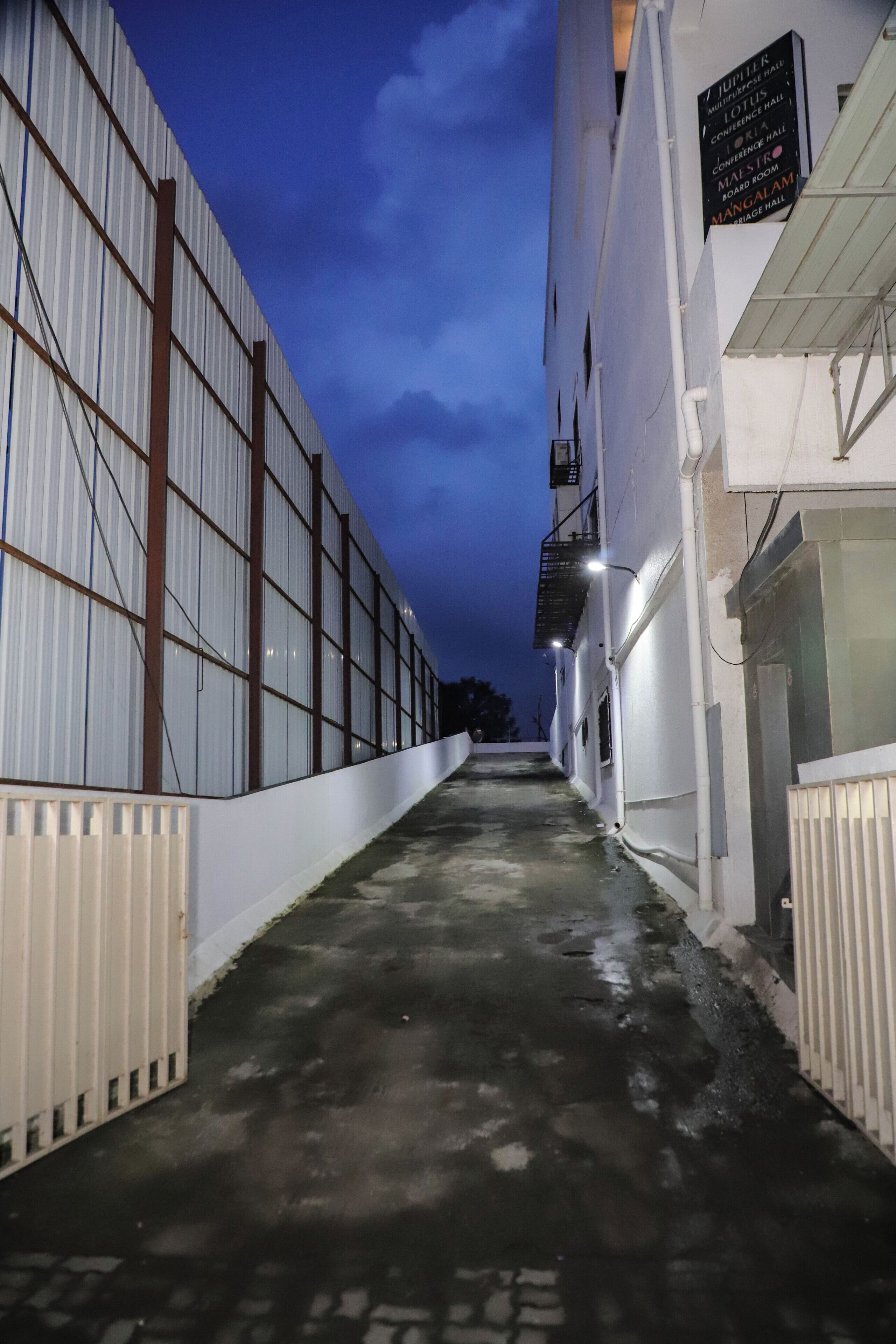 A corridor with a metal fence on one side and a white building with a sign on the other.
