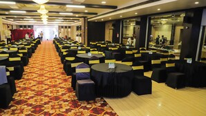 Un salón de banquetes con filas de mesas y sillas, una alfombra estampada y una araña de cristal.