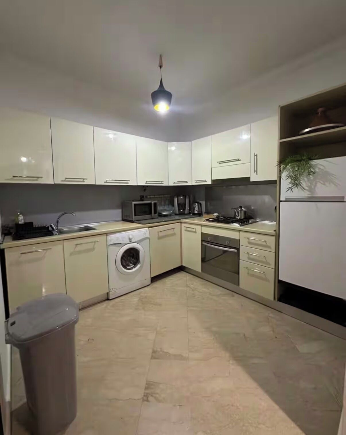 A modern kitchen with white cabinets, a washing machine, a microwave, a stove, and a sink.