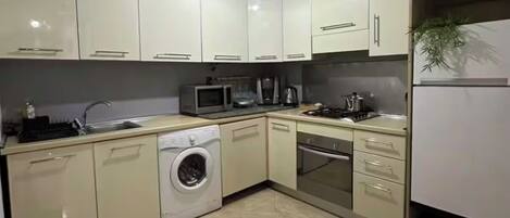 A modern kitchen with white cabinets, a washing machine, a microwave, a stove, and a sink.