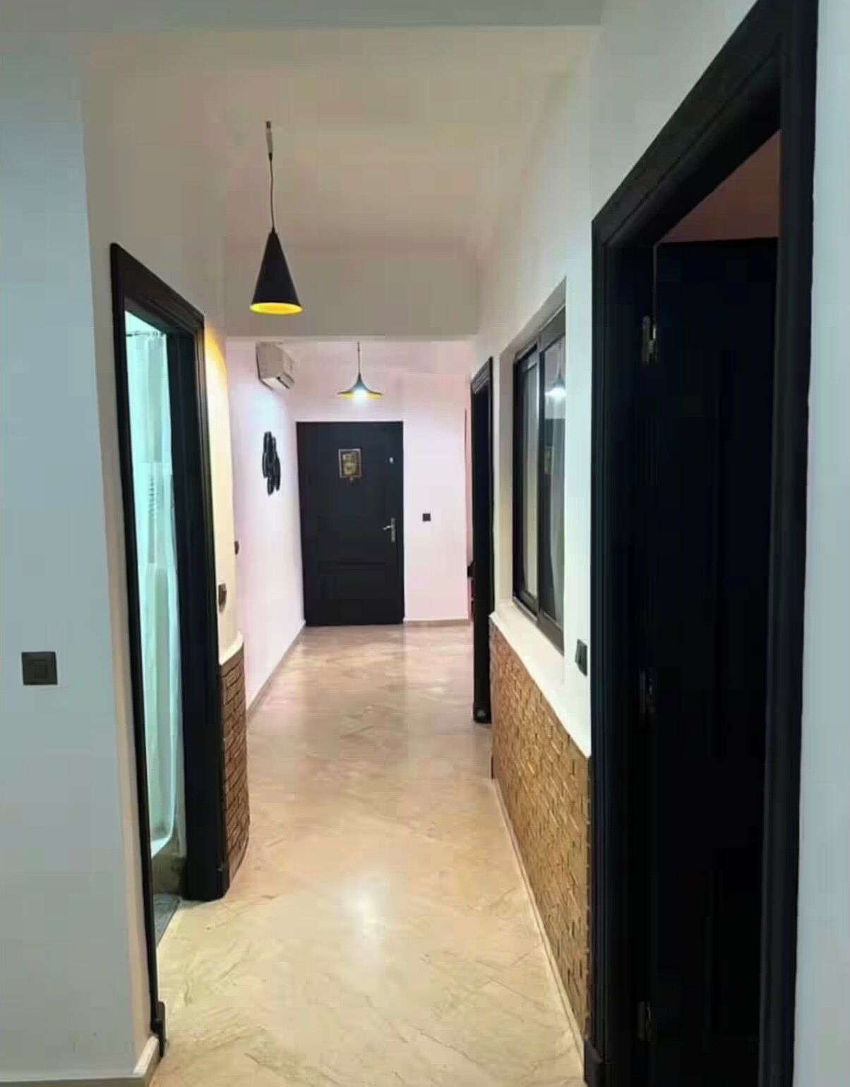 A hallway with a tiled floor, a black door at the end, and a pendant light.