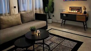 Ein Wohnzimmer mit einer Couch, einem Couchtisch, einem Fernseher der ein Feuer zeigt, einer Pflanze und einem Beistelltisch.